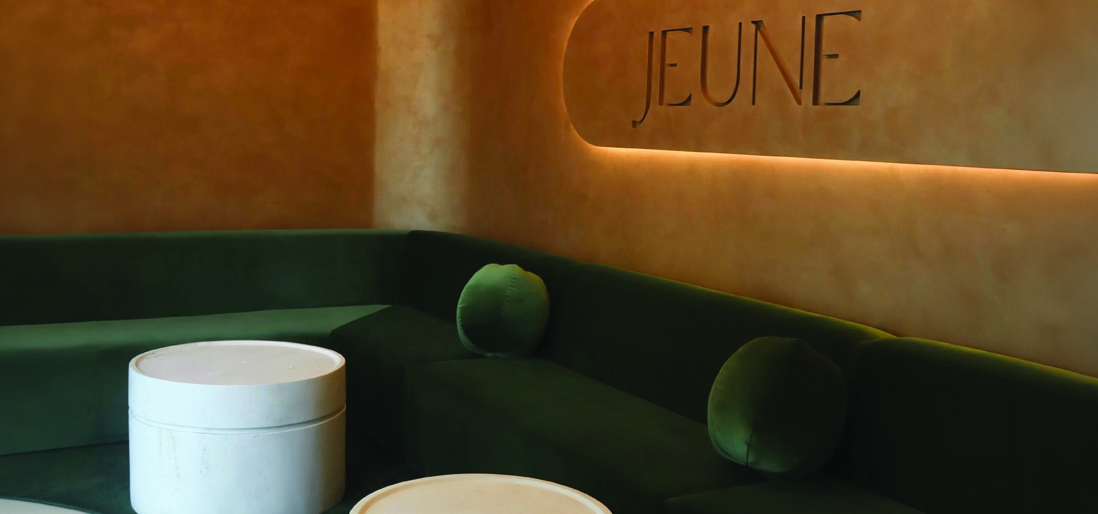 Jeune Aesthetics interior with green velvet seating and illuminated wall logo